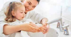 A mother helping her daughter to wash her hands in the bathroom sink.